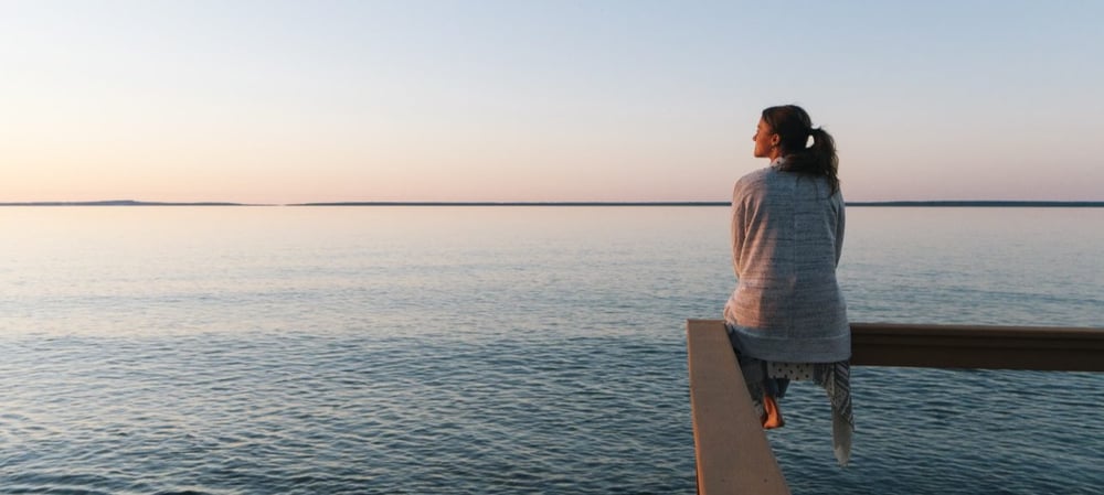 Person sitting on pier looking out at sea during sunset.