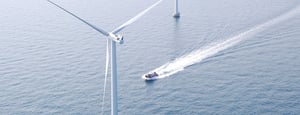Small vessel speeding past offshore wind turbine in open water.