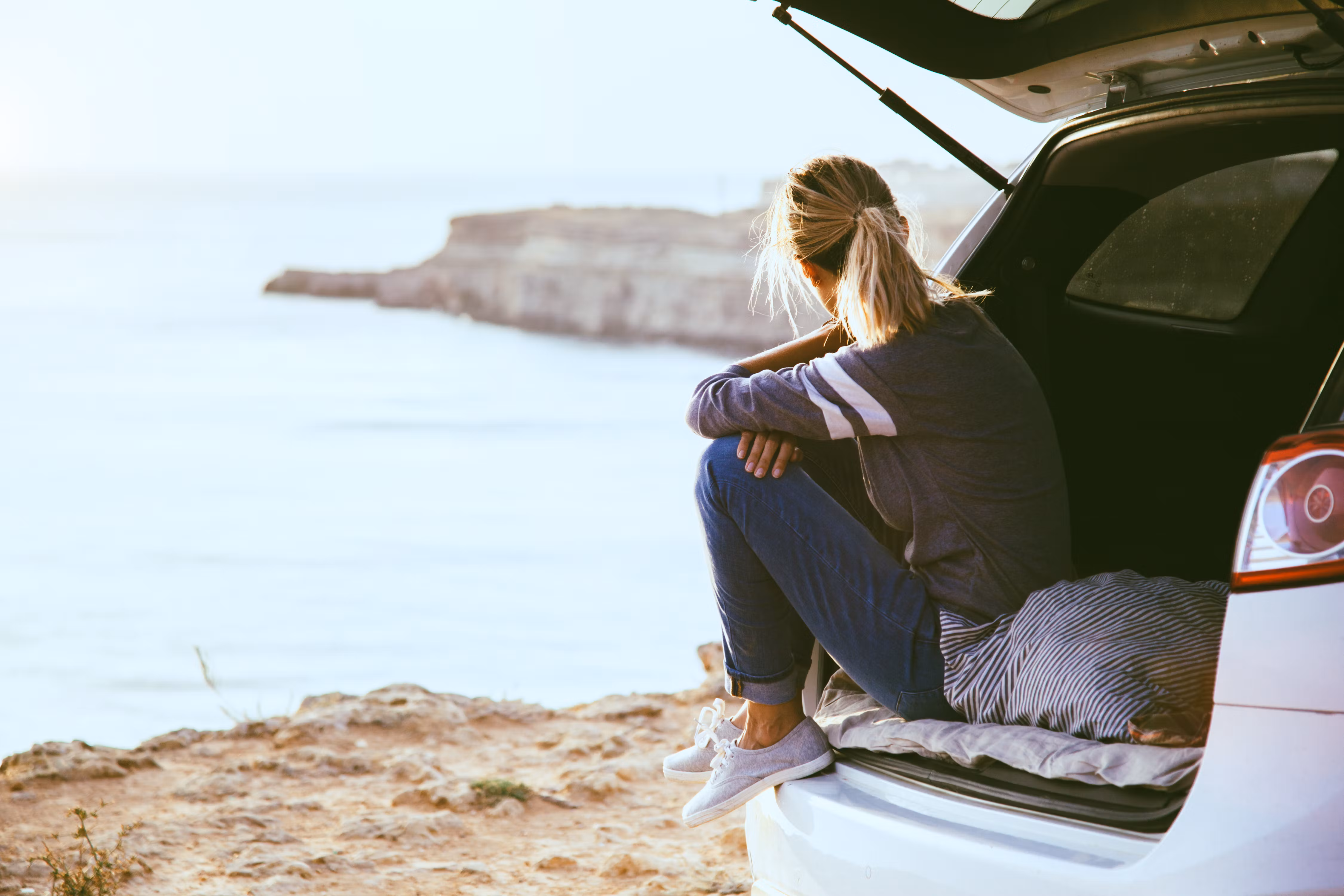 Person sitting in back of car at beach, looking out at sea. Person sitting in back of car at beach, looking out at sea.